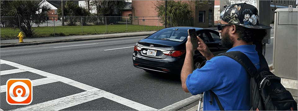 An image of a blind user holding the phone at an intersection using the OKO application to let him know of the walk or don't walk signal is on.